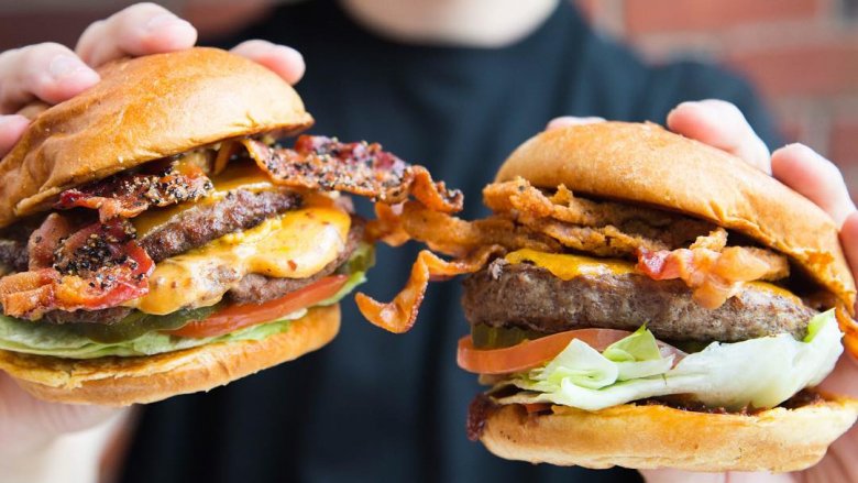 hands holding two large burgers