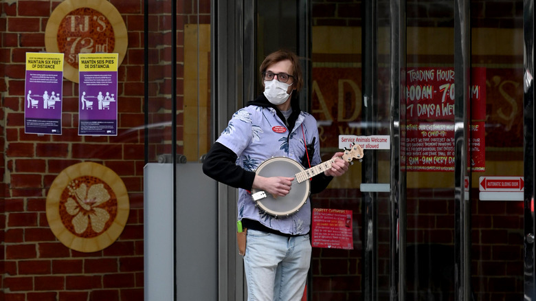 A masked Trader Joes employee in a Hawaiian shirt plays a banjo outside the store