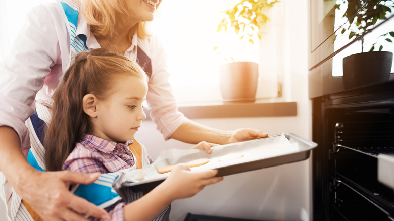 Grandma helps granddaughter put cookies in the oven