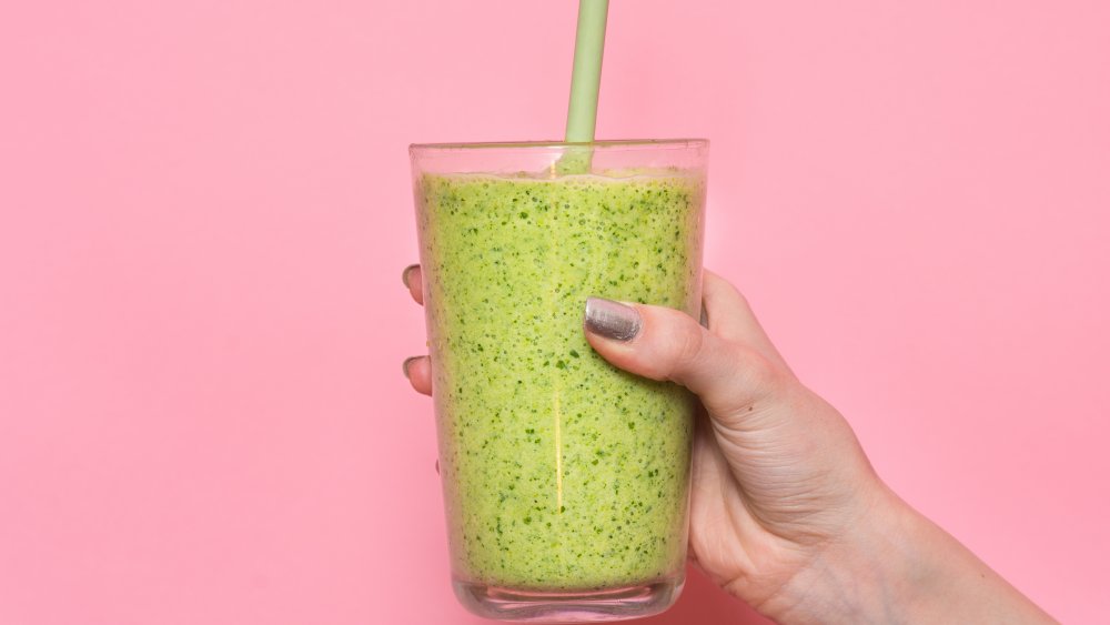 hand holding a green smoothie against a pink wall