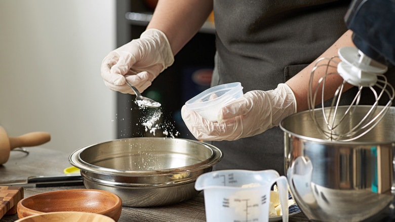 Person adding baking powder to a metallic bowl