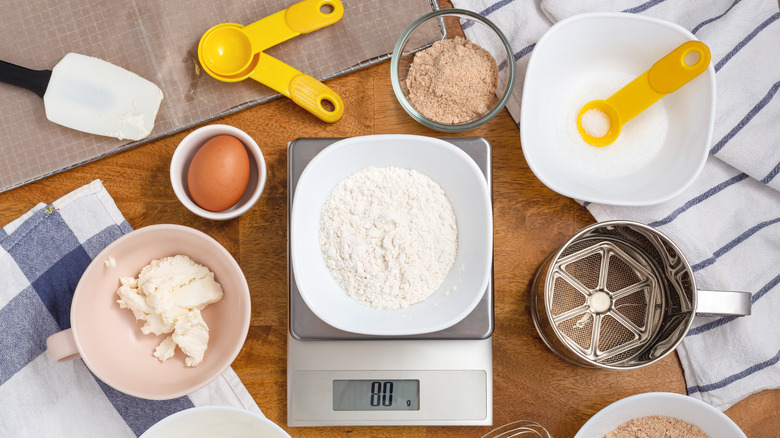 Flour on digital scale with cookie ingredients on wooden table