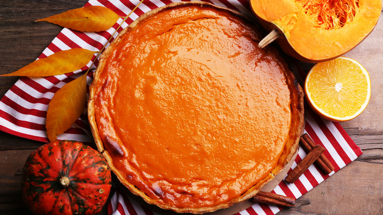 Whole pumpkin pie with pumpkins and napkin