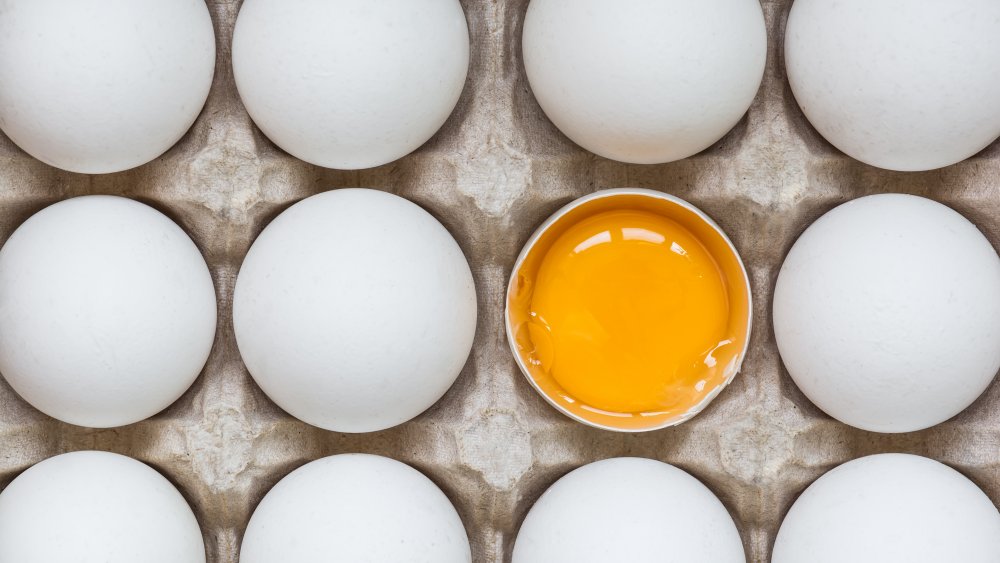 eggs in carton with one broken to show yolk