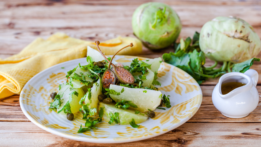 A plate of cooked kohlrabi, with parsley and capers, and surrounded by a sauce, raw kohrabi and a napkin