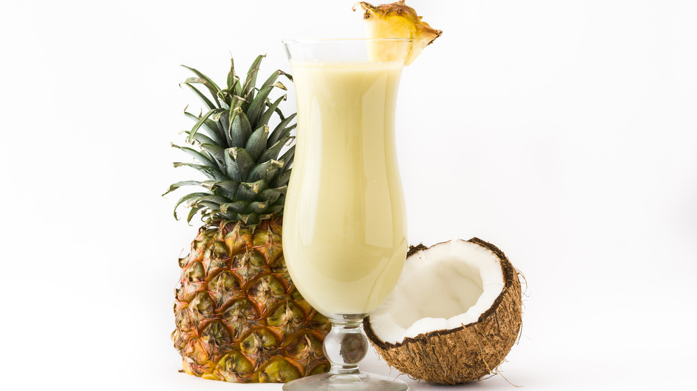 pina colada on white background with pineapple and coconut beside it