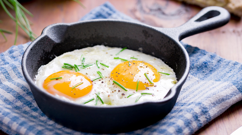 Fried eggs in a pan with salt, pepper, and chopped chives on top