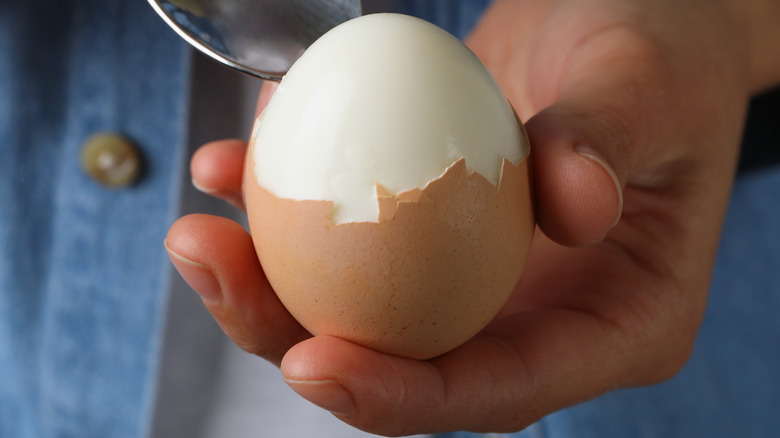 A hand holding a partially peeled boiled egg