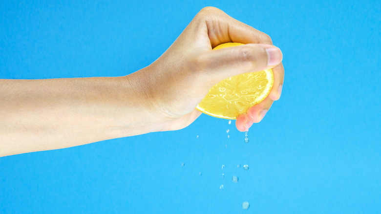 Person squeezing half a lemon with their bare hand.