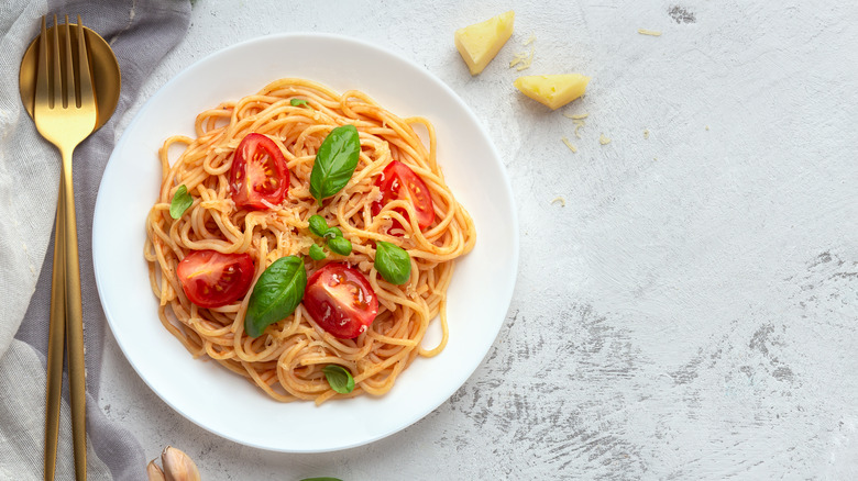 Bowl of pasta with tomatoes and basil next to utensils