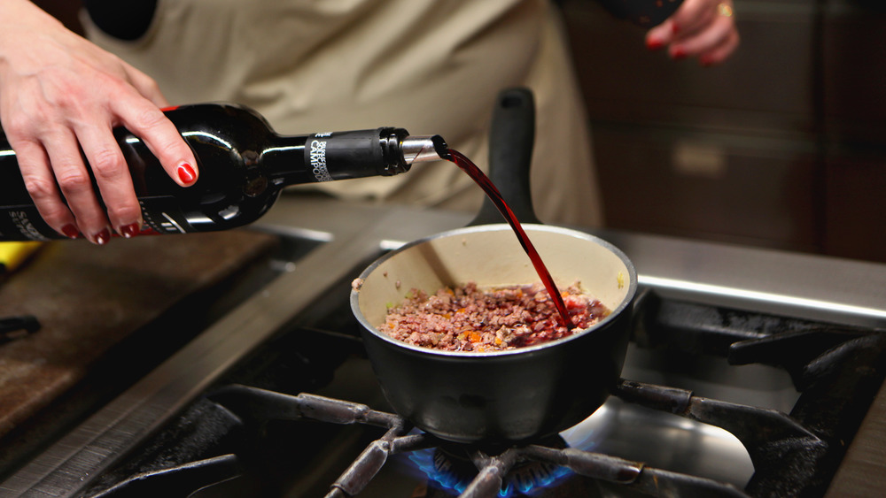 Wine being poured into a pot of bolognese