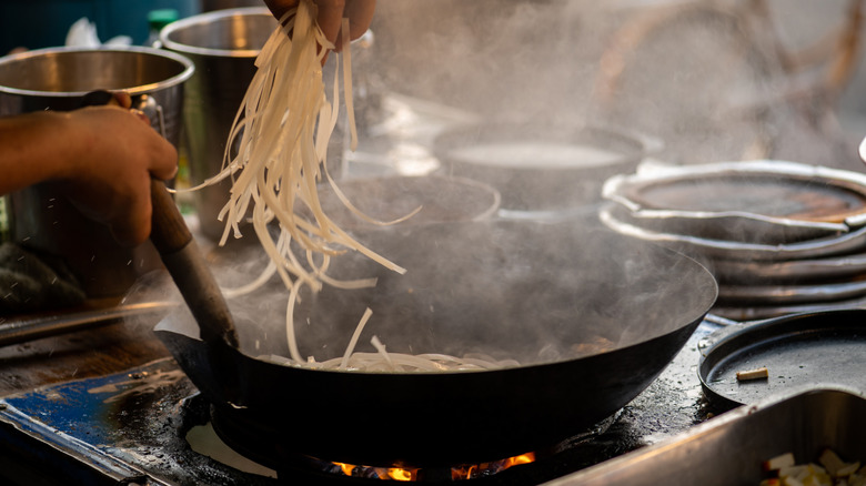 Person adding rice noodles to pan