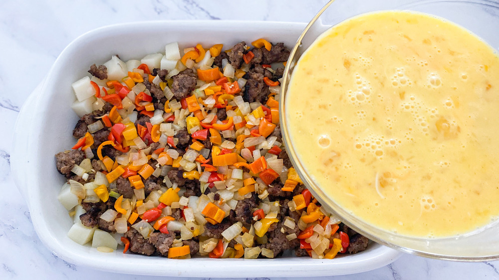 bowl of eggs, milk and cheese over sausage breakfast casserole