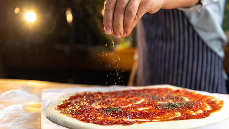 chef putting oregano on pizza