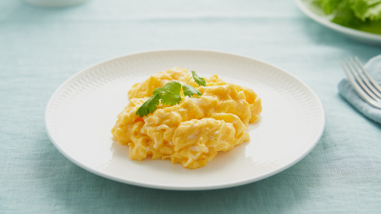 Scrambled eggs on white plate with garnish and fork