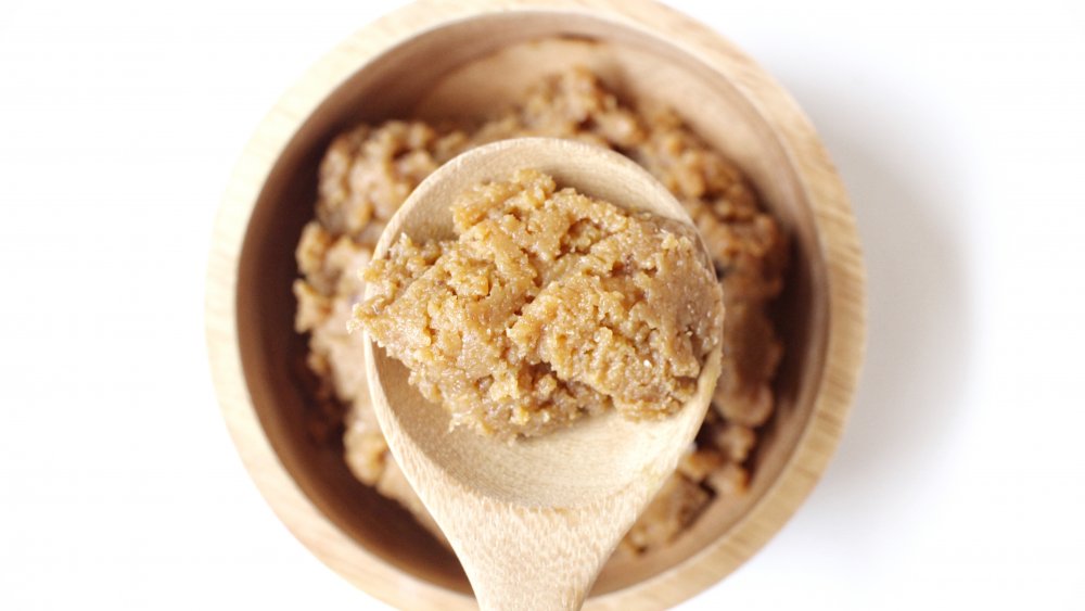 Wooden spoon of light brown-colored shiro miso paste on white background. 