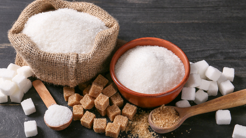 Various types of sugar, white granulated and brown, in cups, spoons and cubes.