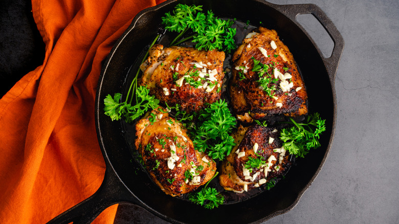 four seared chicken thighs garnished with onion and parsley in a cast iron pan