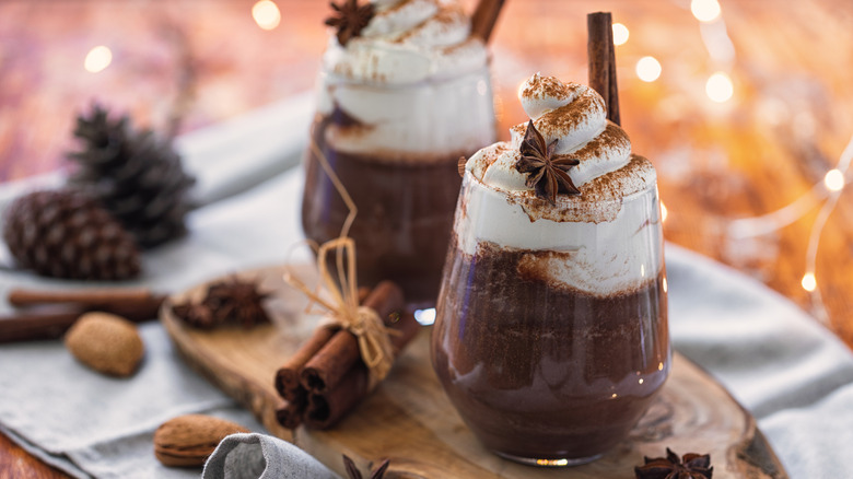 two glass mugs of hot cocoa with whipped cream in festive setting