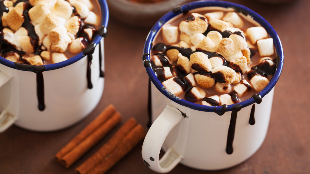 two mugs of hot chocolate with marshmallows and cinnamon sticks 