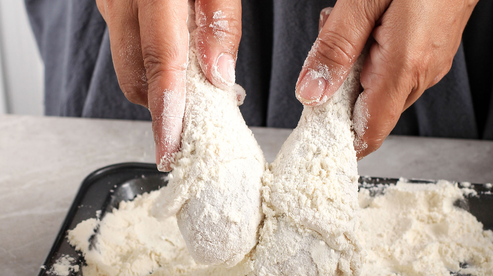 Person making fried chicken with flour