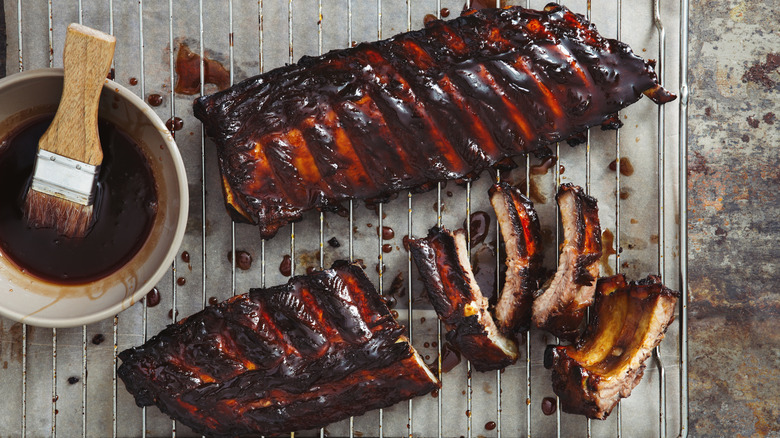 Two racks of ribs on wire rack with bowl of barbecue sauce