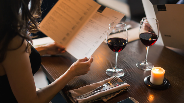 A woman reading a menu with two glasses of red wine