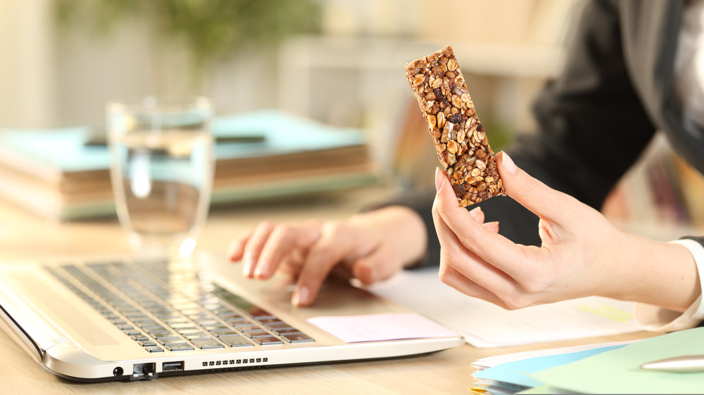 Hands, a computer, and a protein bar.