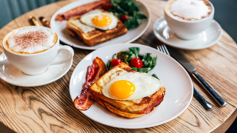 Two plates of eggs on toast with bacon and greens