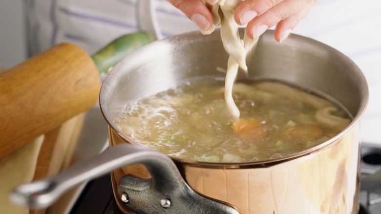 Person adding shredded chicken to pot of water