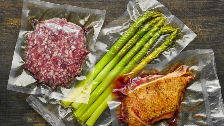 A ground meat patty, asparagus, and pork chop in sealable bags