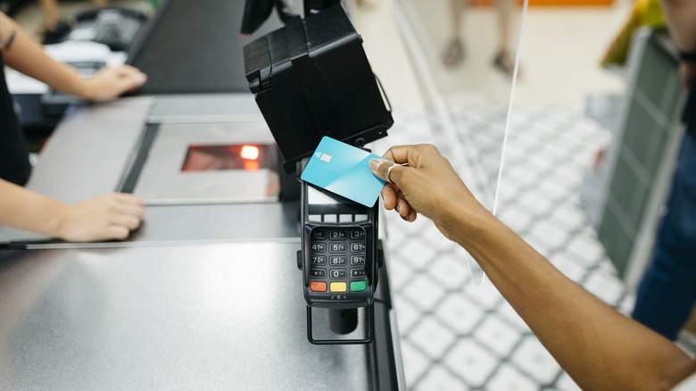 A hand tapping a credit card to pay at the grocery store