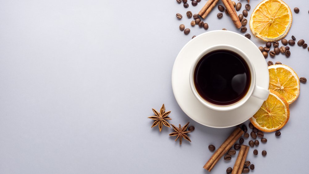 cup of coffee with spices and dried orange around it