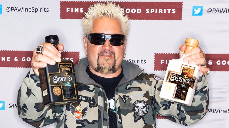 Guy Fieri holds two bottles in a camouflage jacket