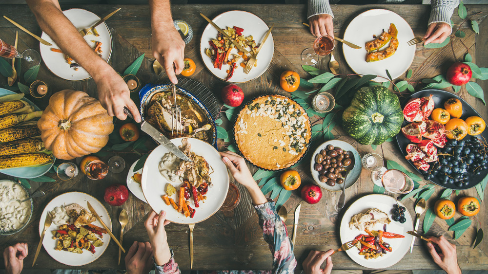 Thanksgiving table with turkey and sides, hands sharing