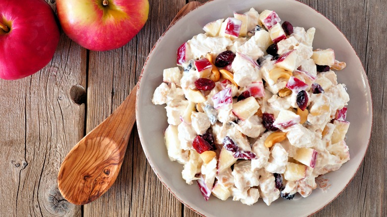 Chicken salad with apples and cranberries next to a wooden spoon