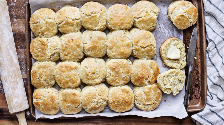 Biscuits on sheet pan with one buttered alongside knife