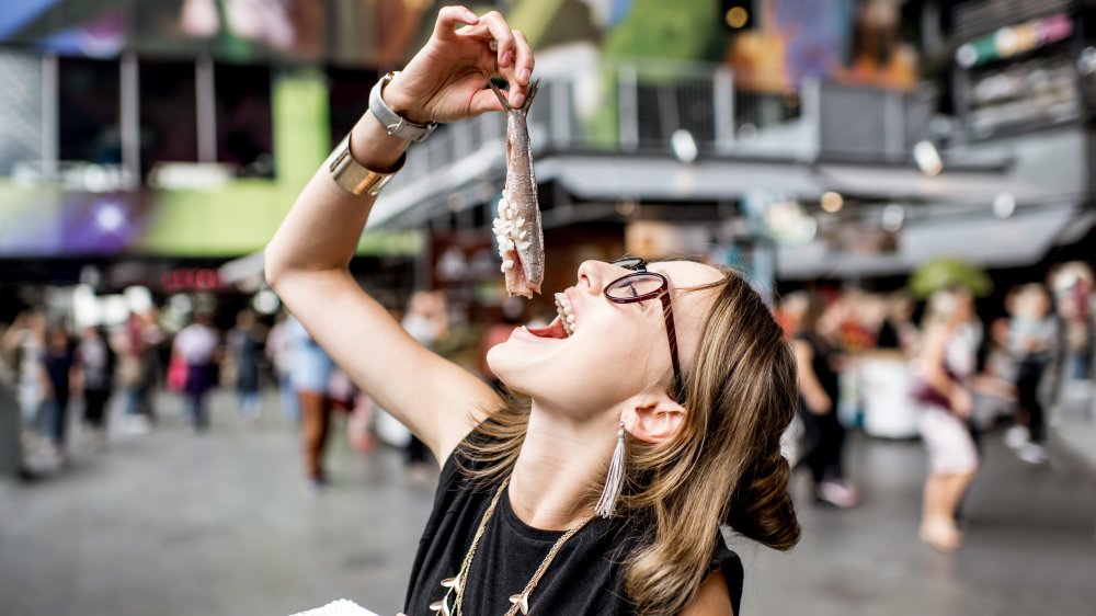 Trendy young woman lowering whole, headless herring into her open mouth