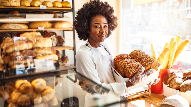 A woman working behind the counter in a bakery holding fresh buns