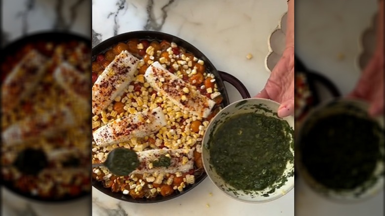 hands pour green sauce over halibut and tomato dish