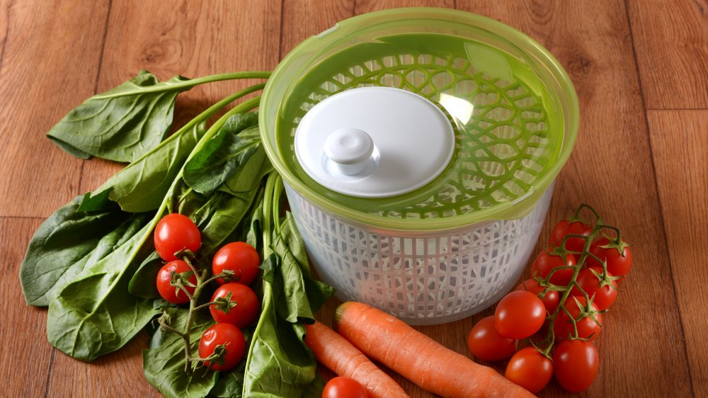 salad spinner on wood countertop with carrots and tomatoes around it