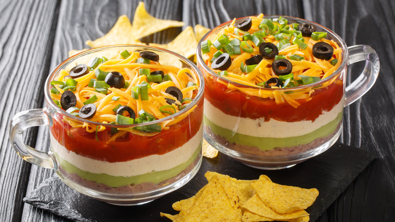 seven layer dip in two glass containers with tortilla chips