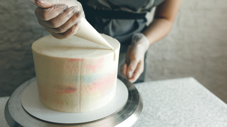 Person frosting a white cake