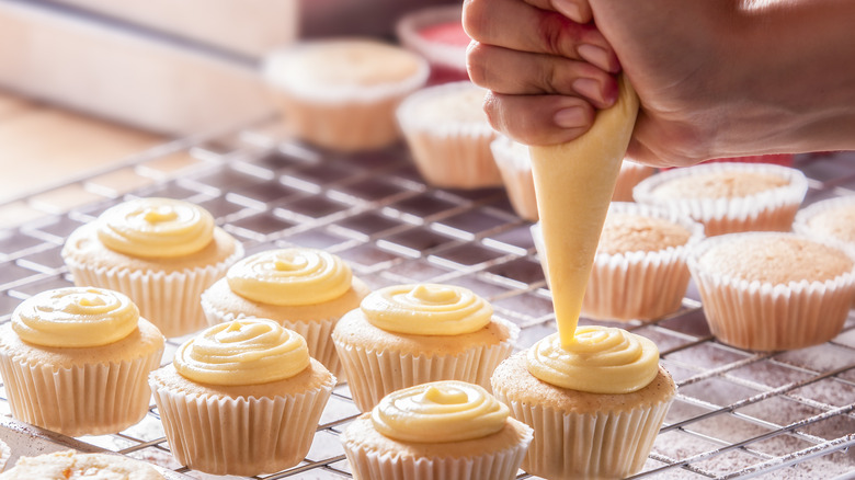 Man is decorating cupcakes with swirls of icing