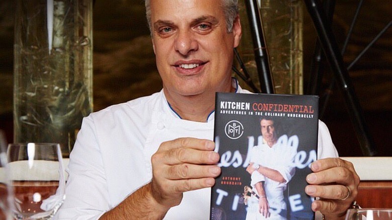 Eric Ripert holding up a copy of Anthony Bourdain's book "Kitchen Confidential"