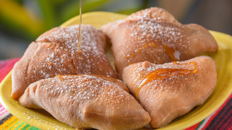 close up of Mexican soapillas on yellow plate with powdered sugar and honey on top