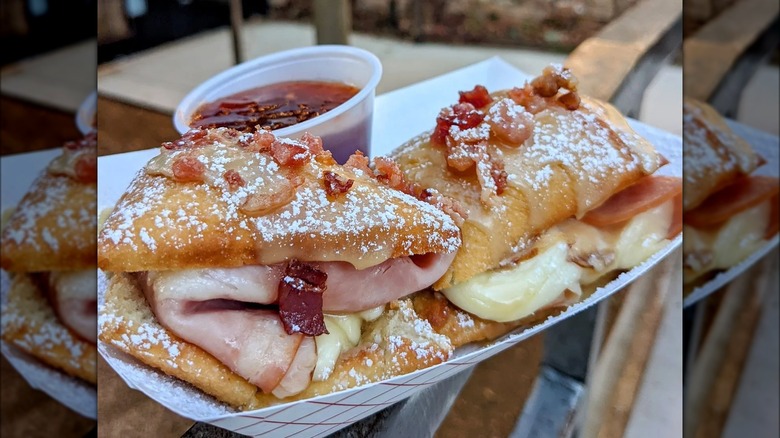 close up of beignet sandwiches in paper boat with plastic cup of sauce on the side