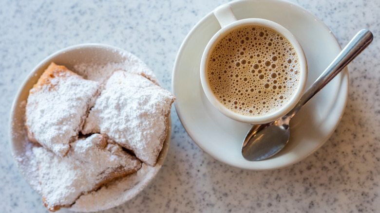 overhead view of Cafe du Monde beignets and cafe au lait on speckled tabletop