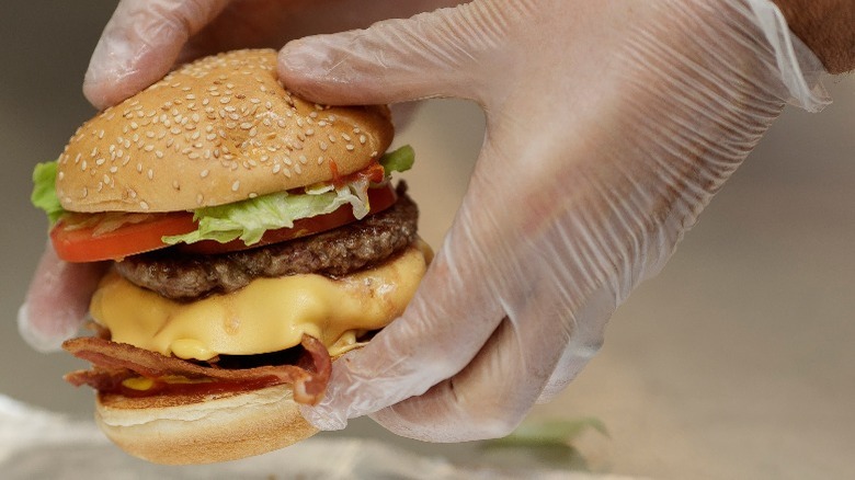 gloved hands holding large cheeseburger