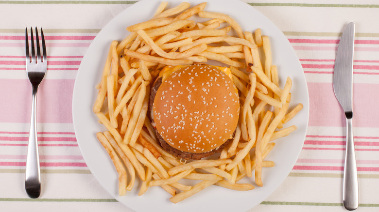 Burger and fries on a plate, fork, and knife.